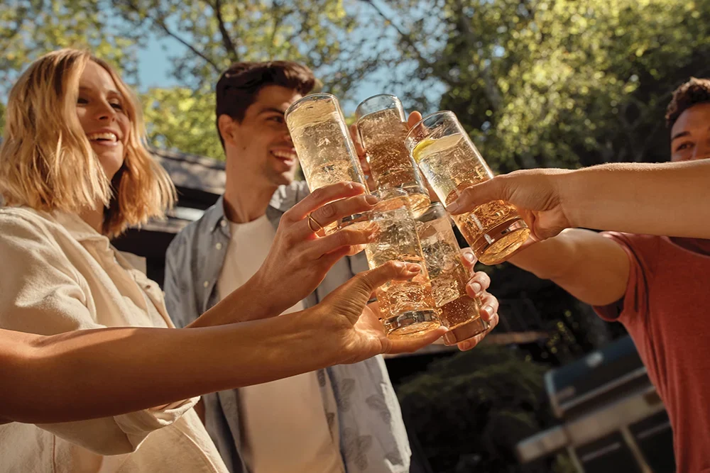 Group of friends clink glasses of mixed drinks together on a Summer day